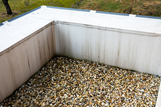 Flat roof corner with gravel ballast and waterproof membrane edge detail on a residential building, showing drainage and roofing construction solution.
