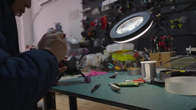Enthusiast soldering small electronic components on a fpv racing drone, working on cluttered workbench with tools and magnifying lamp, enjoying the process of diy electronics assembly and repair