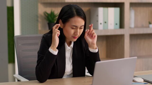 Worried Asian Korean business woman looking laptop hoping crossed fingers office female worker employer Japanese Chinese nervous businesswoman girl computer device gesture pray begging wishing indoors