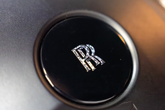A tight close up frames the glossy black steering wheel center with the chrome RR monogram. Shallow depth of field and warm highlights suggest studio lighting and luxury.