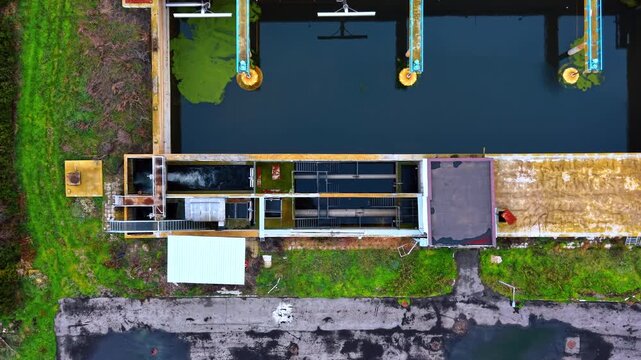 Top down close up of wastewater treatment machinery. Vertical aerial shot of rectangular tanks with water, pipes, and green algae during the purification process.