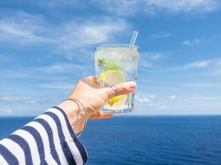 Hand holding a glass of drink against a bright blue sky. Refreshing cocktail moment, summer relaxation and a vacation vibe. Perfect for beverage, travel, and lifestyle marketing campaigns. Close-up © Svetlana