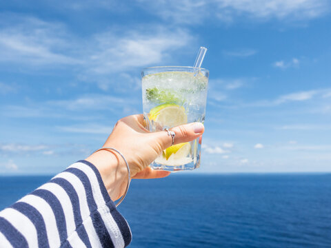 Hand holding a glass of drink against a bright blue sky. Refreshing cocktail moment, summer relaxation and a vacation vibe. Perfect for beverage, travel, and lifestyle marketing campaigns. Close-up