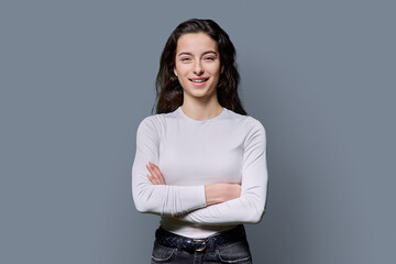 Beautiful young woman with crossed arms looking at camera on grey background
