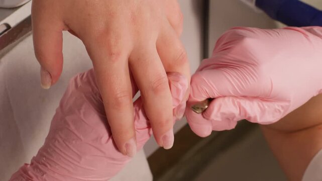 Vertical video. Nail manicure. Salon procedure. Beautician female master hands in protective gloves cutting cuticle skin on clients finger using forceps for beauty.