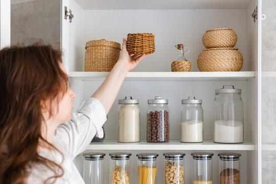 A young woman puts dishes in a cupboard, the housewife tidies up the kitchen, food storage