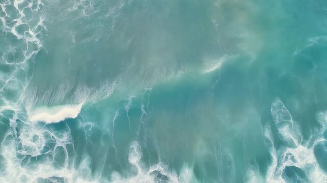 Aerial view of ocean waves crashing on the shore with sea foam and blue water