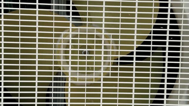 Closeup Air Conditioner Fan Grille Showing Rotating Blades During Maintenance Inspection, Dust Accumulation On Plastic Housing, Exposed Motor And Wiring, Shadowed Background, High detail.