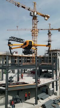 Construction site inspection using yellow industrial drone. Workers in safety vests monitoring automated survey at building development. Panning and tilting camera movement.