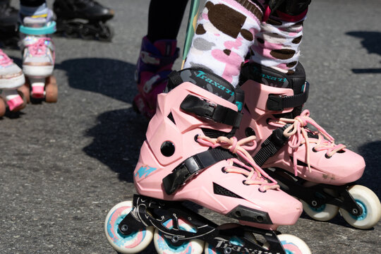 A low-angle close-up captures vibrant pink Traxart inline skates on rough asphalt pavement.