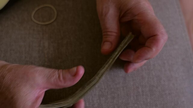Close-up of a pensioner finishing counting small banknotes, neatly rolling the cash and fastening it with a rubber band. 
