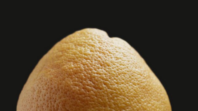Unpeeled grapefruit rotating at black background. Grapefruit peel texture. Close-up in 4K, UHD