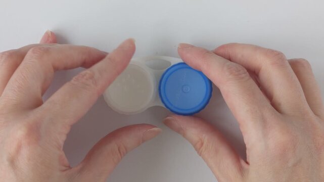Woman holding case with contact lenses on white background, closeup. Woman's hands unscrew the lid of a contact lens case. Concept for eye care and hygienic lens storage