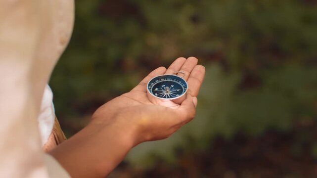 A woman with light skin holds a compass in her hand, looking at it with interest. She explores a natural setting, engaged in outdoor activities.