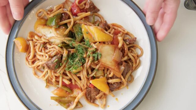 Serving Guiru lagman, noodles with beef and stewed vegetables in sauce, close-up, top view, Uyghur cuisine dish