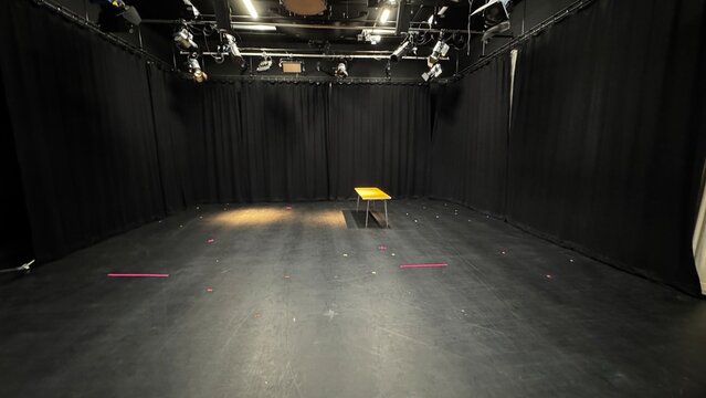 Empty black box theater studio stage with a single table under lighting rigs