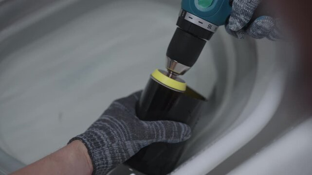 Top view of craftsman grinding sharp edge of cut glass bottle with rotary tool in basin of water to create drinking glass, upcycling and handmade craft concept, close-up. Shooting in slow motion.
