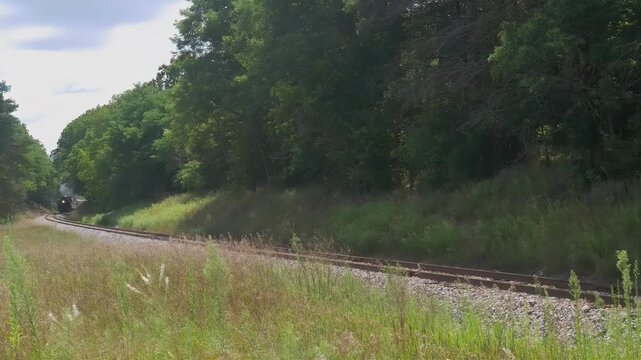 Vintage steam train chugging along a scenic railway track through lush green countryside