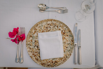 Elegant dining table setting with ornate plate, silver cutlery, white napkin, and vibrant pink...