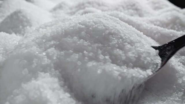 In bright light, glistening sugar crystals cascade smoothly from spoon. Each grain swirls and settles in soft, inviting mound, ready to sweeten delicious treats.