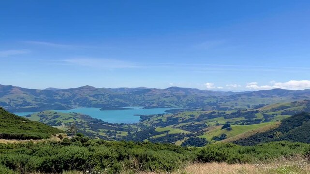Peninsula view from top of a hill. Robinsons Bay near Akaroa, New Zealand. Blue sky and green landscape with peninsula in the background. Sunny summer day in the South Island.