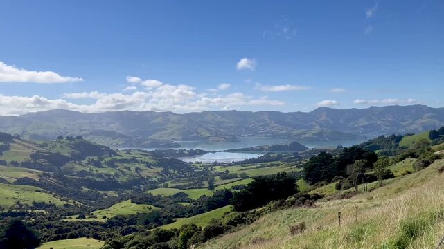 Peninsula view from a green hill. Akaroa in New Zealand. Blue sky and green hills landscape. Summer and sunny day in the South Island.