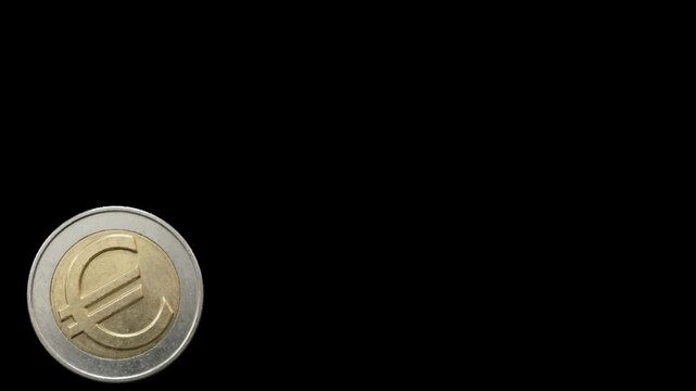 Close-up of a small gold coin with engraved symbol on dark background.