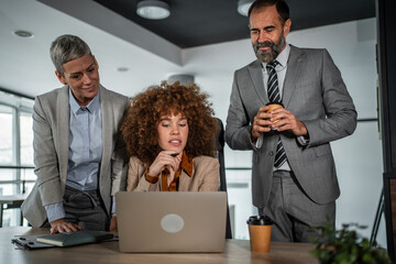 Diverse business professionals collaborating on laptop in modern office