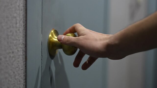 Hand turns brass doorknob to open door, revealing dark interior space