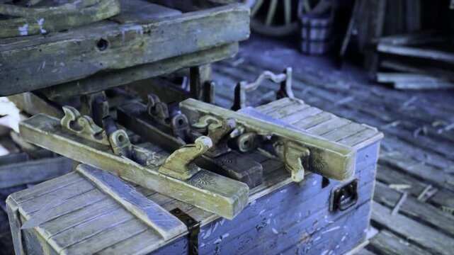Closeup vintage wooden clamp on bench, weathered tool chest and metal vise with patina, dim shop light highlights textured grain, scattered bolts and hinge,