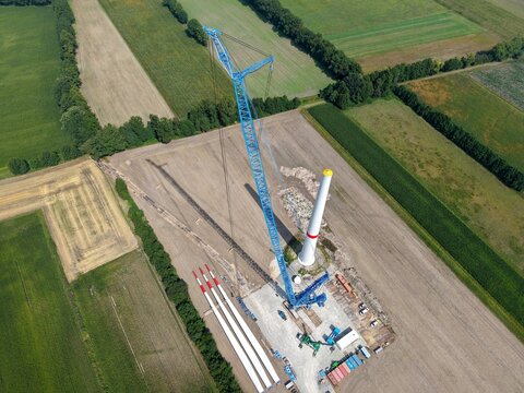 A lattice boom crawler crane prepares for the installation of a new wind turbine in the wind farm; aerial view, preparation, construction site, energy transition