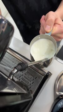 Barista froths milk using steam wand for coffee preparation in cafe setting