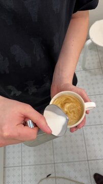 Person pours milk into coffee cup, creating latte art in kitchen setting