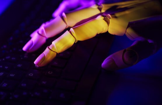 Robotic hand typing on computer keyboard in neon light