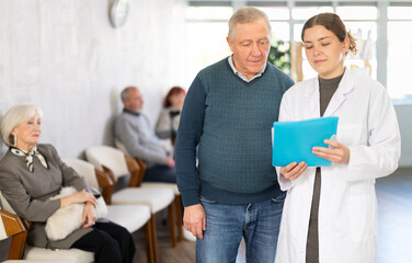 Serious nurse or doctor discussing treatment with senior male patient in public healthcare facility