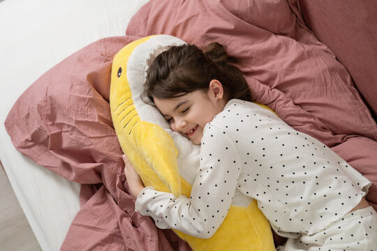 Girl in pajamas cuddling plush toy in cozy bed