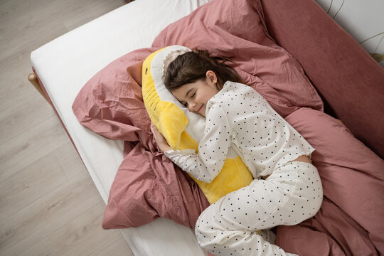 Girl in pajamas cuddling plush toy in cozy bed
