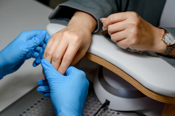 Nail technician applies manicure treatment to client's hand in salon