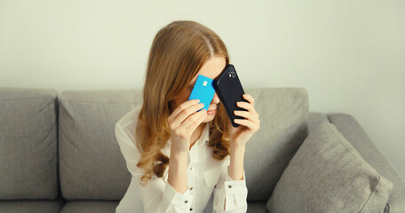 Upset young woman with smartphone, credit bank card, internet fraud, problems with online payments