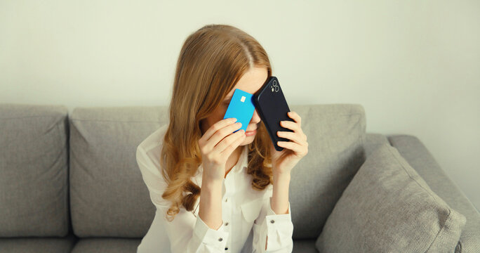 Upset young woman with smartphone, credit bank card, internet fraud, problems with online payments