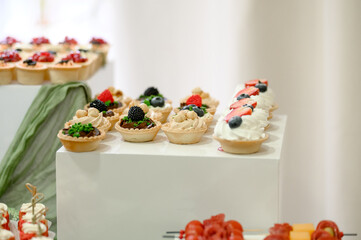 Assorted mini tarts with fresh fruits displayed on a white pedestal
