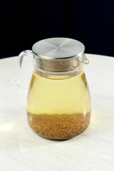 Glass pitcher with herbal tea infusion on marble table surface