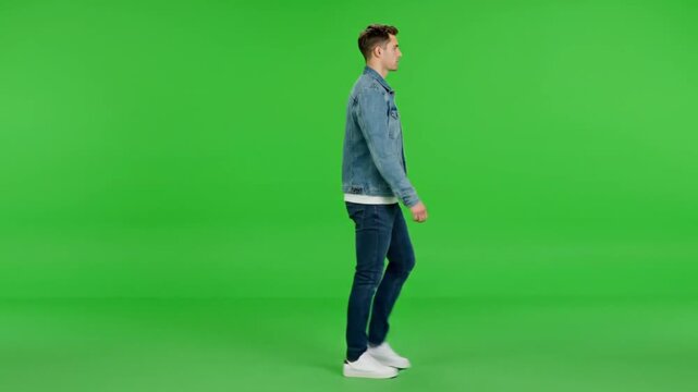Young man walking in denim jacket and jeans on green screen background in studio lighting for advertising