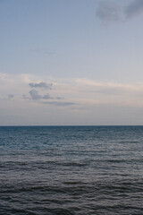 Fototapeta premium Calm ocean water under a cloudy sky at dusk near the shoreline