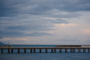 Fototapeta premium Long pier extending over calm ocean waters under cloudy sky