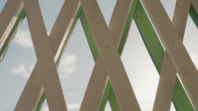 Closeup wooden lattice sunlight sky vista peeling green paint, rough grain, radiant sunflare through diamond openings, soft clouds, gentle breeze implied, domestic setting, home memory, quiet