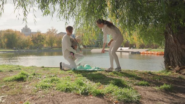 Family joy beneath gentle autumn sunlight. Newly married couple shares tender moments by serene waters. Cherished family scene with smiling couple and newborn near tranquil lake and weeping willow
