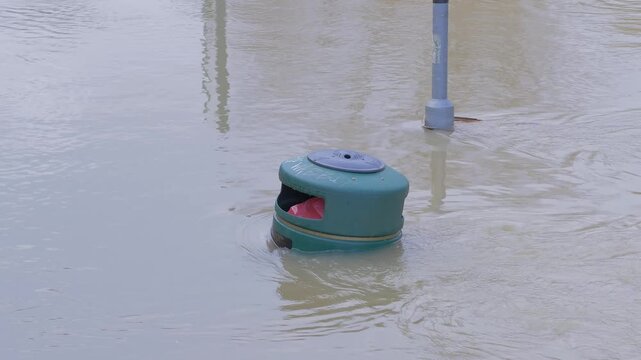 submerged waste refuse rubbish bin and lamppost in fast flowing muddy brown water, swirling currents and eddies
