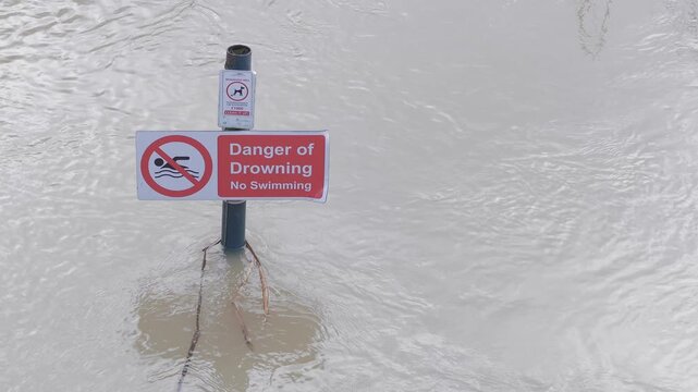 submerged sign in fast flowing river flood, rippling muddy brown water, danger of drowning, no swimming warning