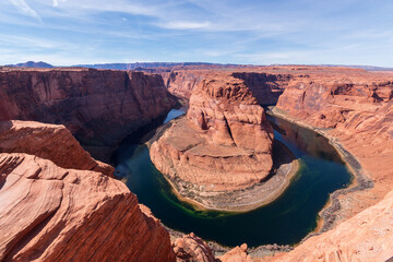 Horseshoe Bend in Arizona featuring the dramatic U-shaped curve of the Colorado River winding around towering red sandstone cliffs under a clear blue sky.